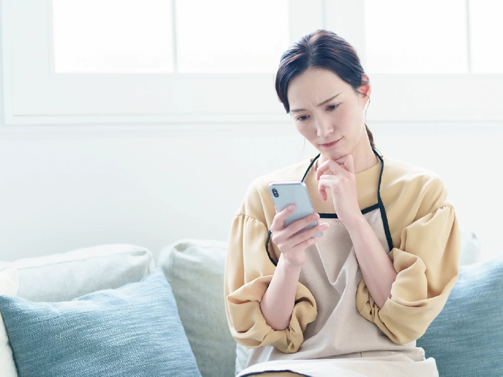 スマホを見ながら悩んでいるお母さん