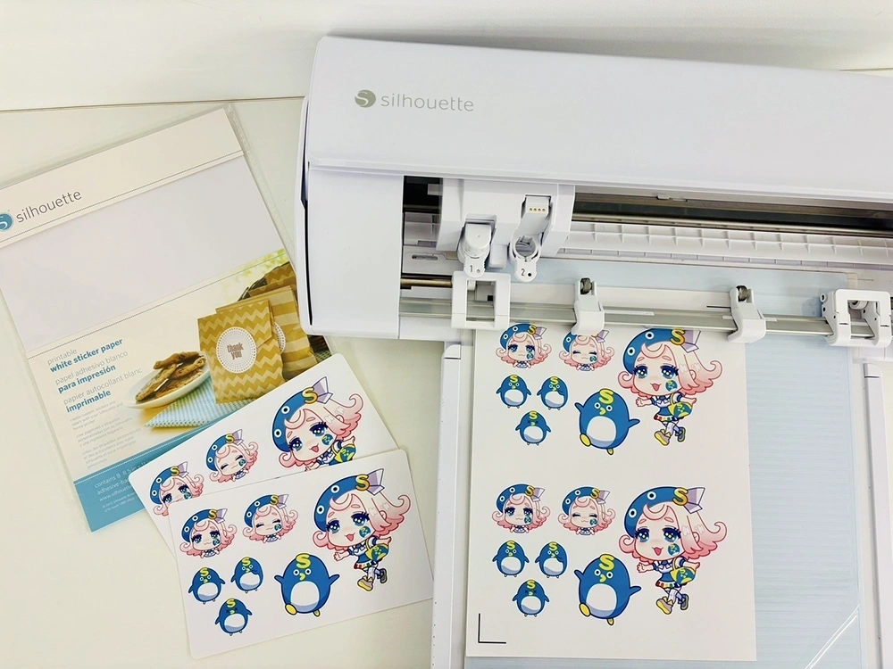 カッティングマシンでキャラクターシールを制作中。ペンギンなどのデザインが並ぶ。