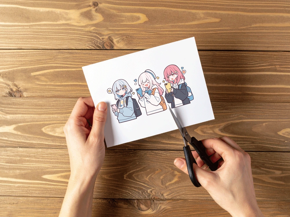 木製の机の上で、手が白紙をハサミで切っている様子。