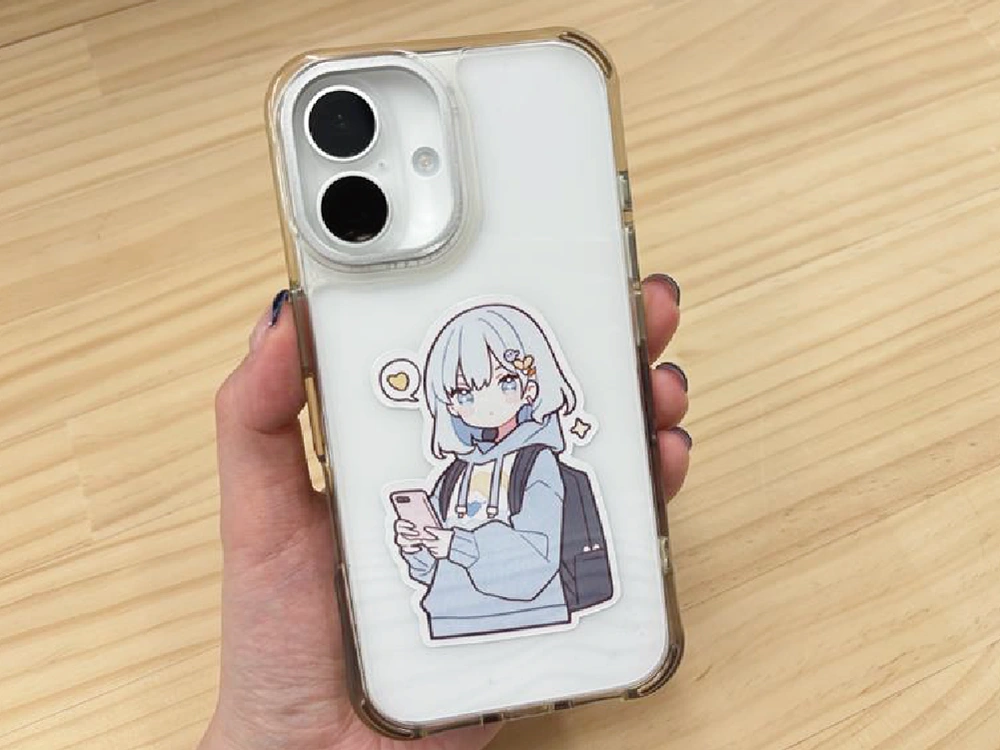 スマートフォンケースの裏に挟まれたアニメ風キャラクターのステッカー。手に持たれている。