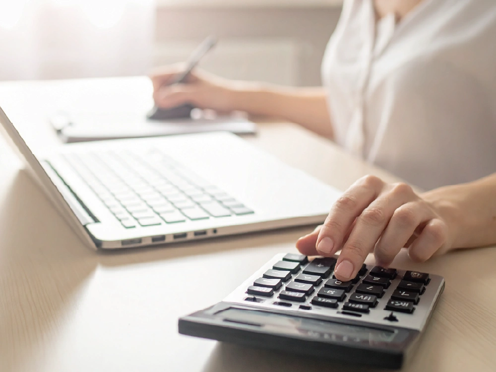 ノートPC前で電卓とペンを使いながら書類作業をする手元。