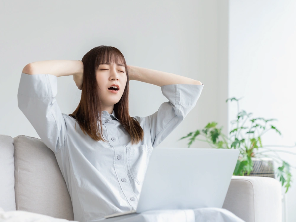 ソファに座り、手を頭の後ろに置いて目を閉じながら悩んでいる人物。