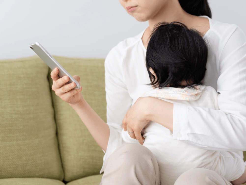 赤ちゃんを抱っこしながらスマホを見るママ